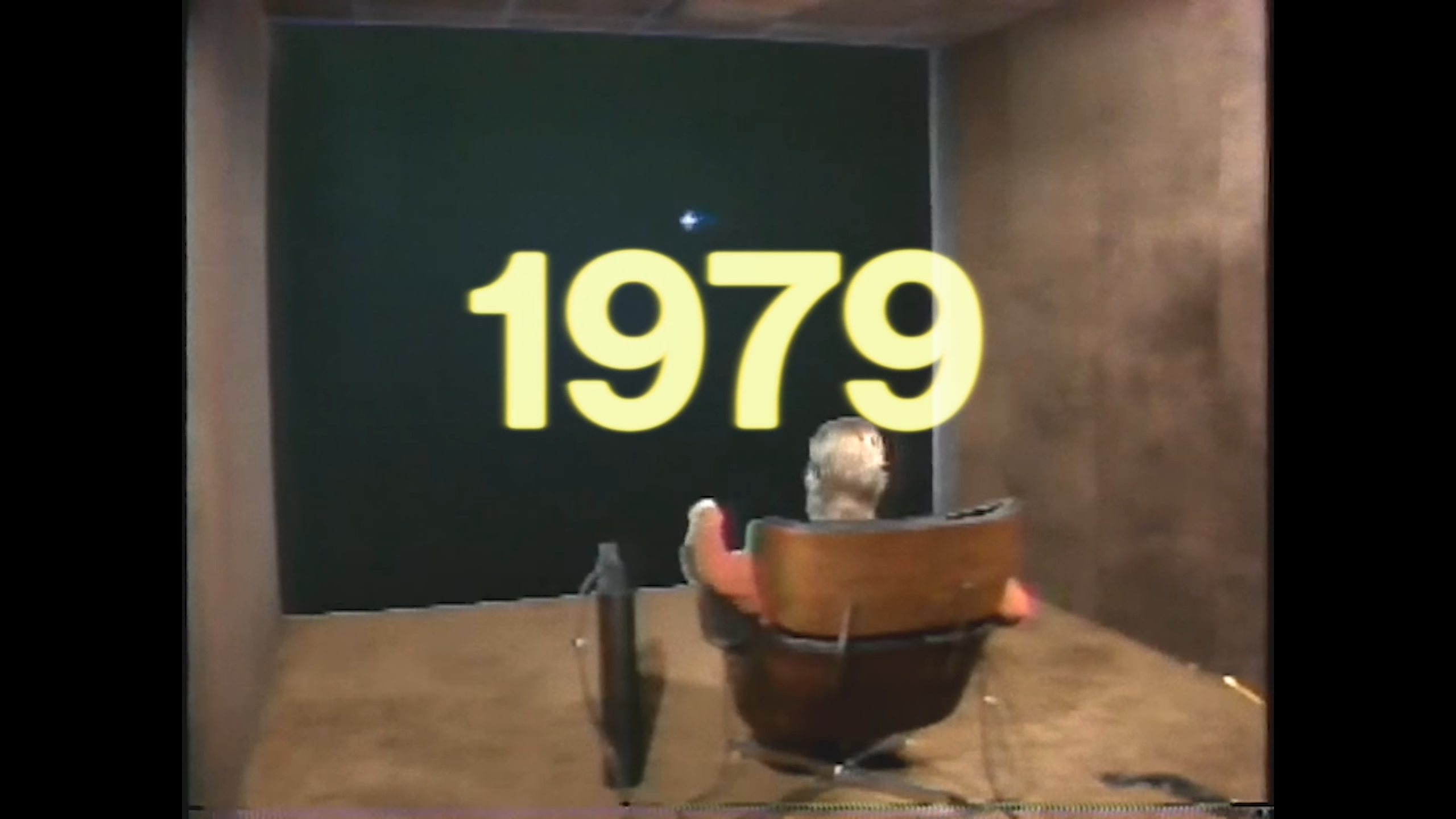 Unaltered launch-film frame: 1979, a seated person facing a large screen.