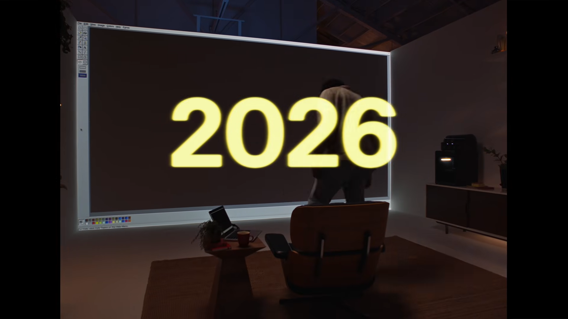 Unaltered launch-film frame: 2026, a lounge chair facing a large software interface.